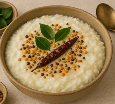 A bowl of South Indian curd rice garnished with curry leaves, dried red chili, mustard seeds, and chana dal, served in a rustic ceramic bowl.
